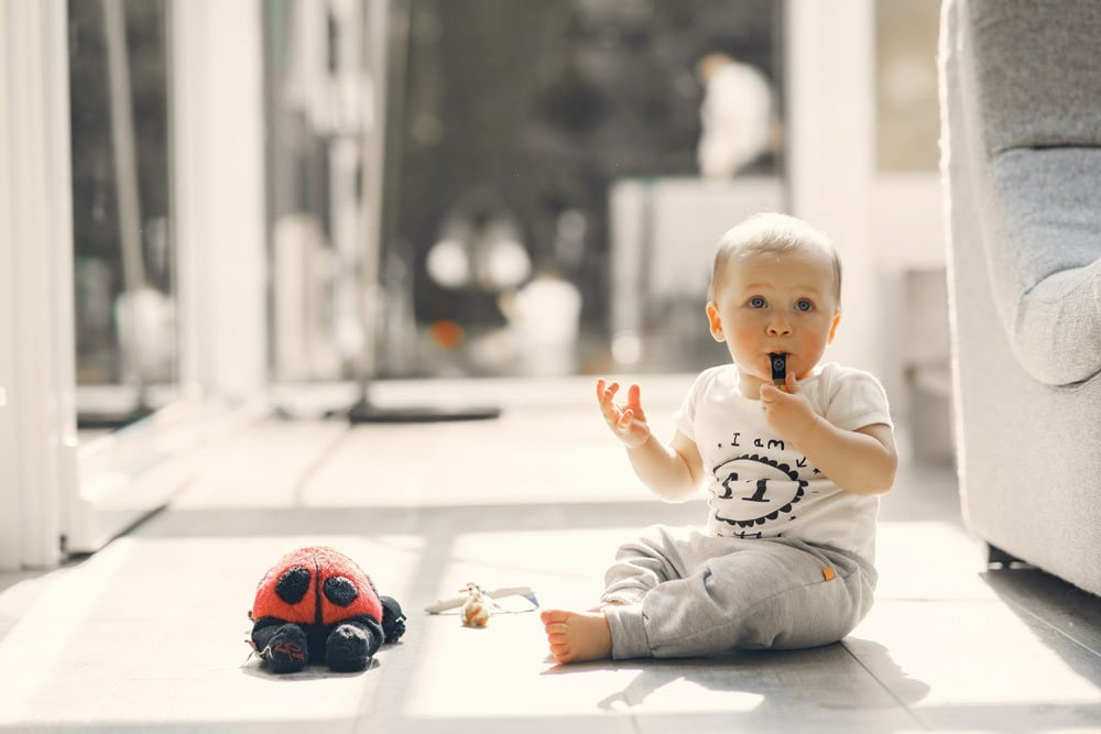 Small Whistle Baby sitting on white floor with ladybug toy