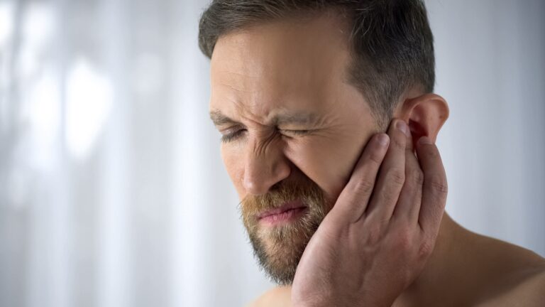 Man holding his aching ear, suffering from otitis, sudden hearing loss, close up