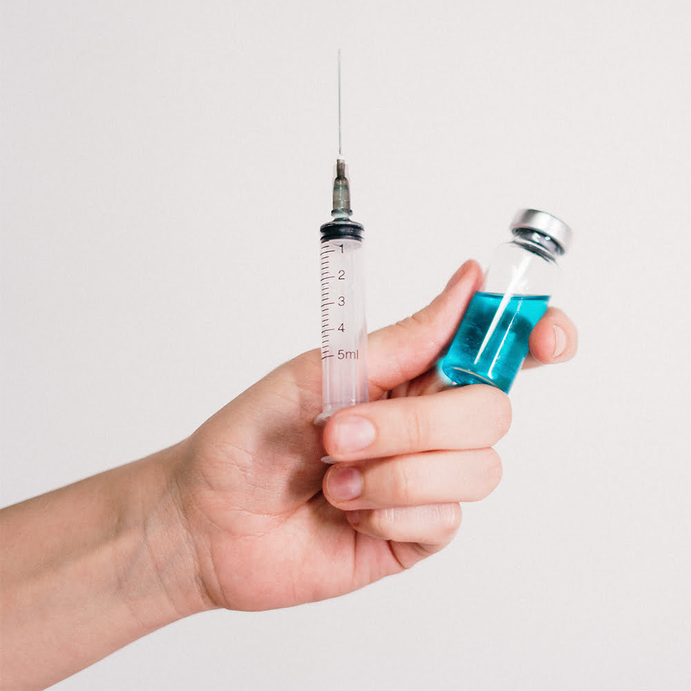 Closeup of hand holding a syringe and a small bottle with blue liquid