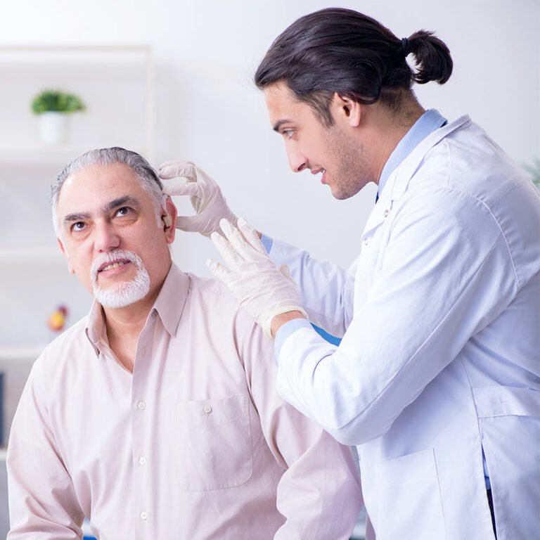 Doctor adjusting hearing aid on middle-aged male patient