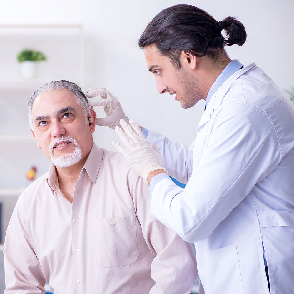 Doctor adjusting hearing aid on middle-aged male patient