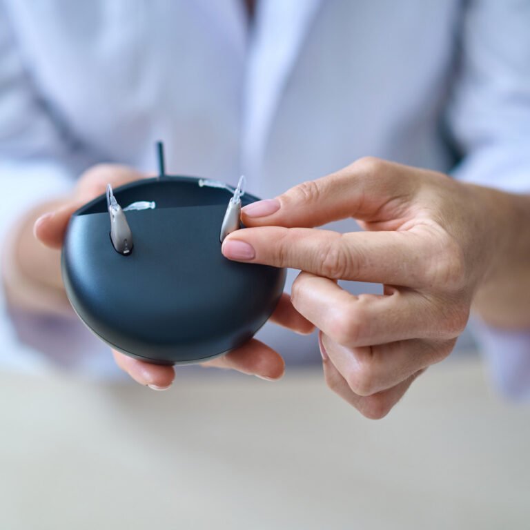 Hearing aid dispenser showing off a pair of hearing aids docked inside their charging station