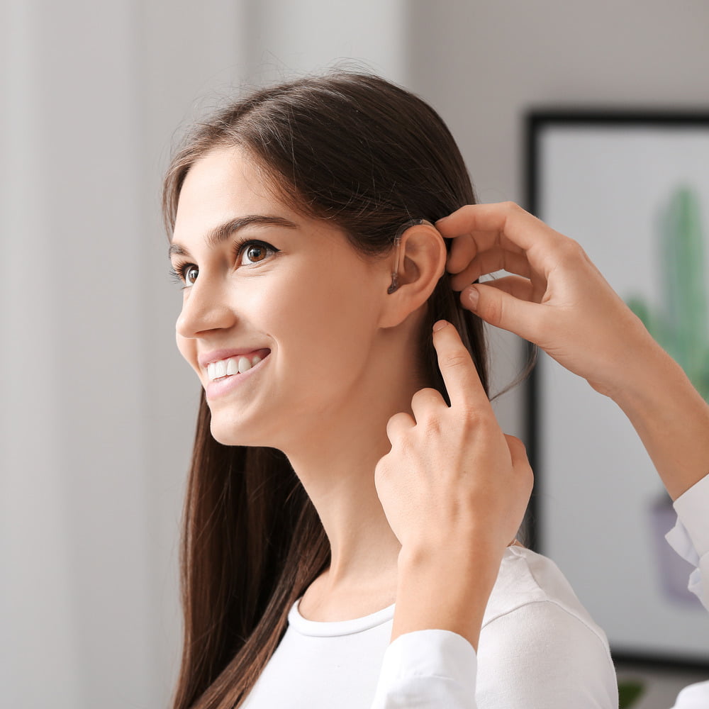 Young woman with long brown hair smiling while having a hearing aid fitted