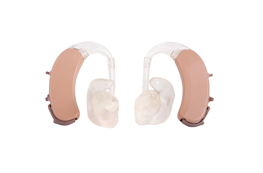 Two beige-coloured hearing aids with domes on white background