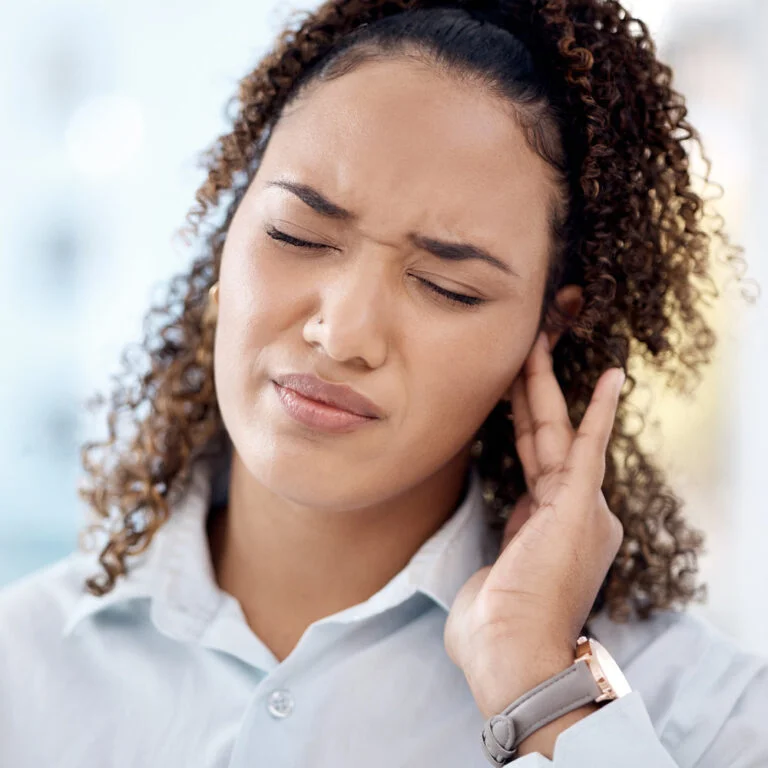 Woman holding hand up to ear, facial expression suggests discomfort- likely ear pain or tinnitus.