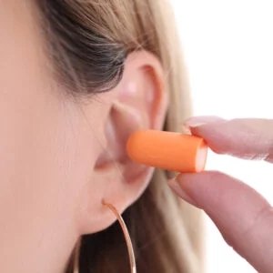 Closeup of person inserting orange earplug into their ear.